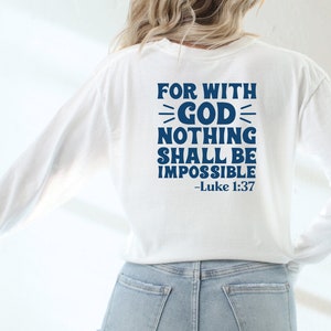 K&ouml;nnte beinhalten: Wei&szlig;es Langarmshirt mit blauem Text, der "For with God nothing shall be impossible - Luke 1:37" lautet.