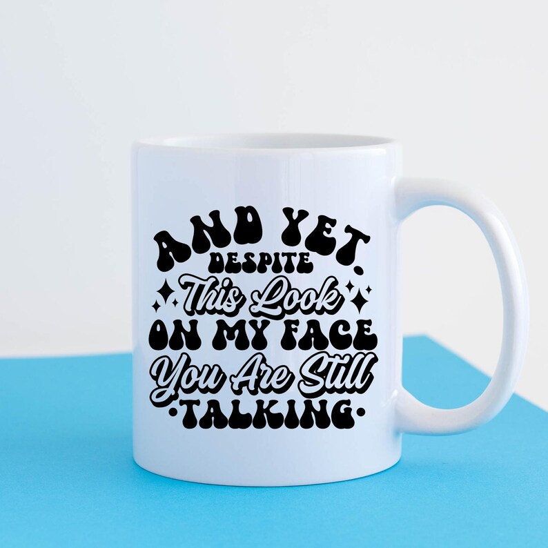 May include: White ceramic mug with a black graphic that reads "And yet, despite this look on my face, you are still talking."