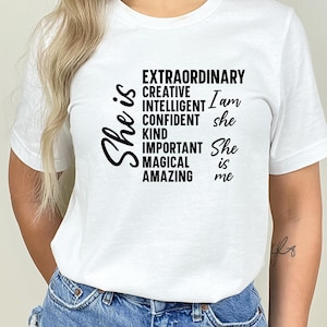 May include: White t-shirt with black text that reads "She is Extraordinary, Creative, Intelligent, Confident, Kind, Important, Magical, Amazing. I am she. She is me."