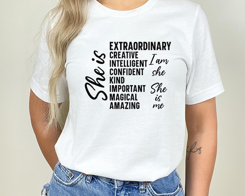 May include: White t-shirt with black text that reads "She is Extraordinary, Creative, Intelligent, Confident, Kind, Important, Magical, Amazing. I am she. She is me."