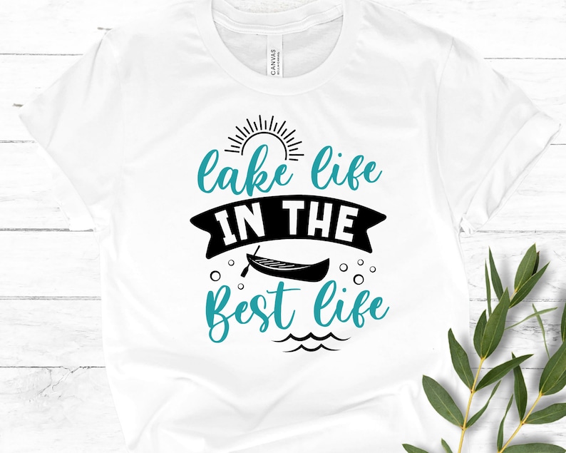 May include: White t-shirt with black text that reads "lake life in the best life". The text is surrounded by a sun, a canoe, and water waves.