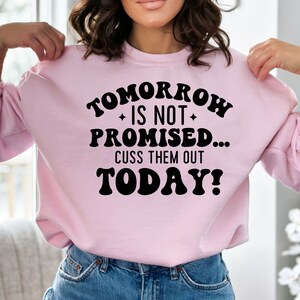 May include: Pink sweatshirt with the text "Tomorrow is not promised... Cuss them out today!" in black.