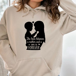 May include: A beige hoodie with a black silhouette of a mother and son hugging. The text "The love between a mother and a son is FOREVER" is printed below the silhouette.