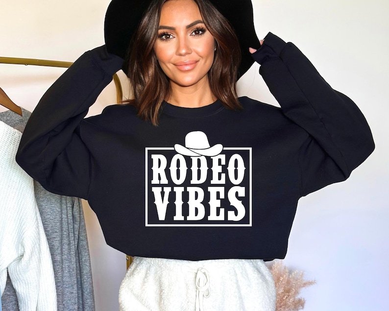 Op de afbeelding: Zwart gecropped sweatshirt met een witte afbeelding van een cowboyhoed en de tekst "Rodeo Vibes".