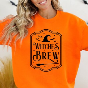 May include: Orange sweatshirt with a black graphic of a witch's hat and the text "Witches Brew" in a decorative frame.