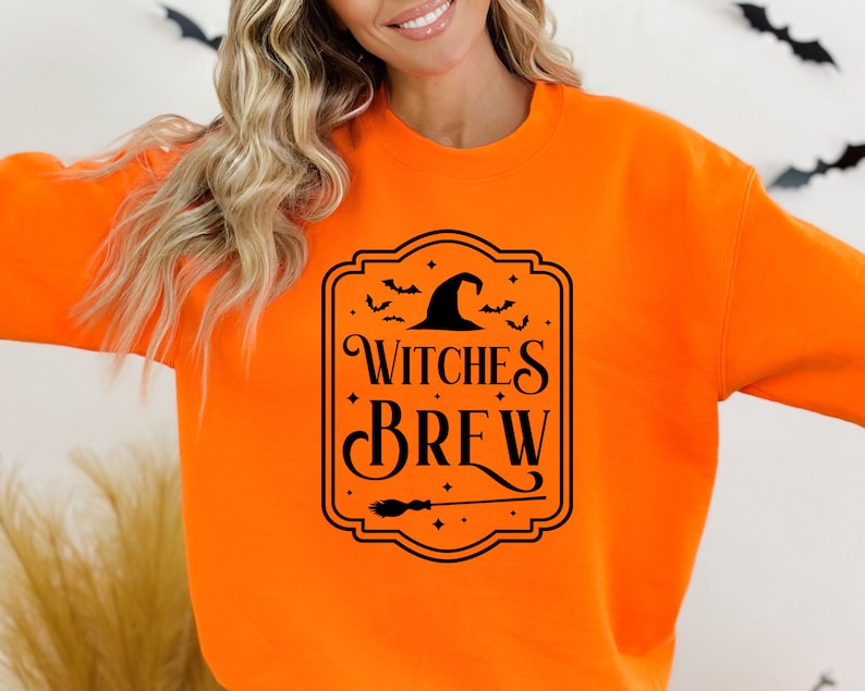May include: Orange sweatshirt with a black graphic of a witch's hat and the text "Witches Brew" in a decorative frame.
