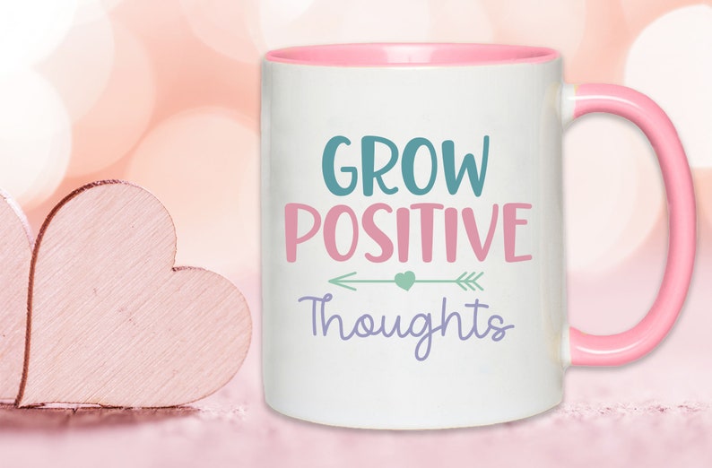 May include: White ceramic coffee mug with a pink rim and handle. The mug has a motivational quote that reads "Grow Positive Thoughts" with an arrow and a heart graphic.