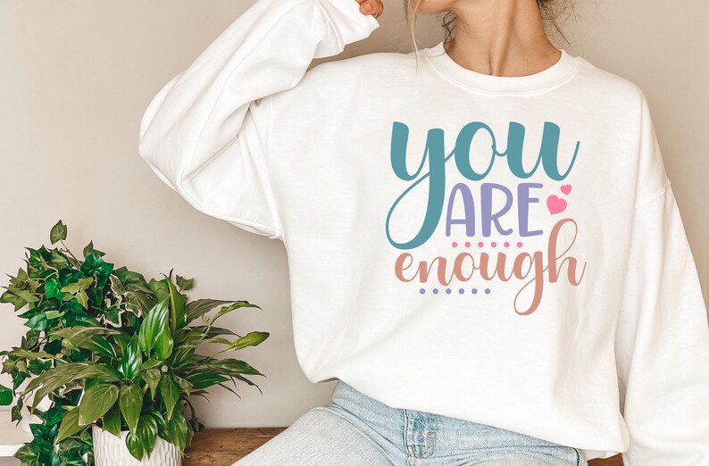 May include: White sweatshirt with the text "you are enough" in colorful lettering with pink hearts.