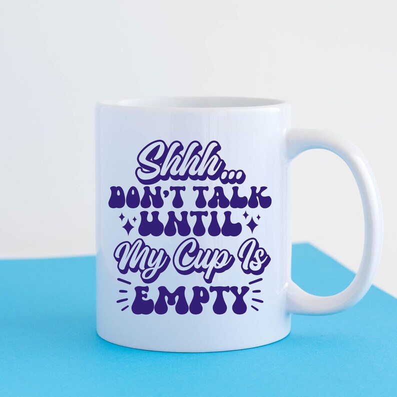 May include: White ceramic mug with a purple design that says "Shhh... Don't talk until my cup is empty".