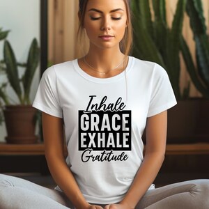 May include: White t-shirt with black text that reads "Inhale Grace Exhale Gratitude".