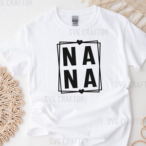 May include: White t-shirt with a black graphic design that says "NANA" in a square frame with hearts.