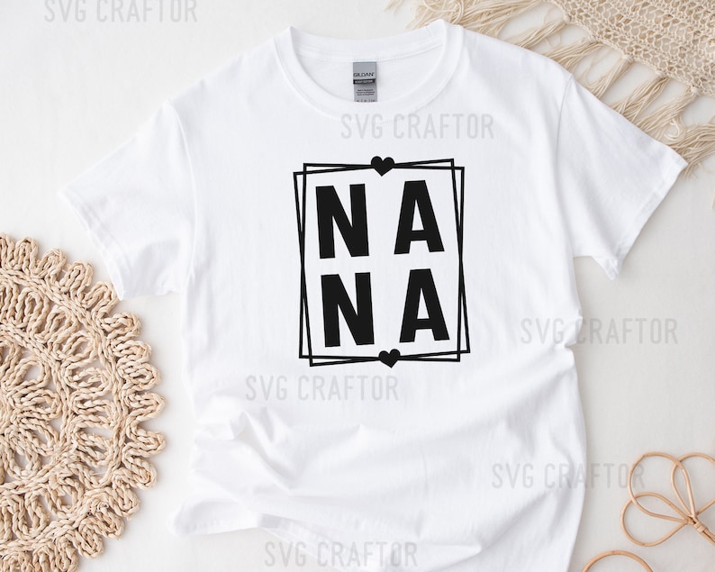 May include: White t-shirt with a black graphic design that says "NANA" in a square frame with hearts.