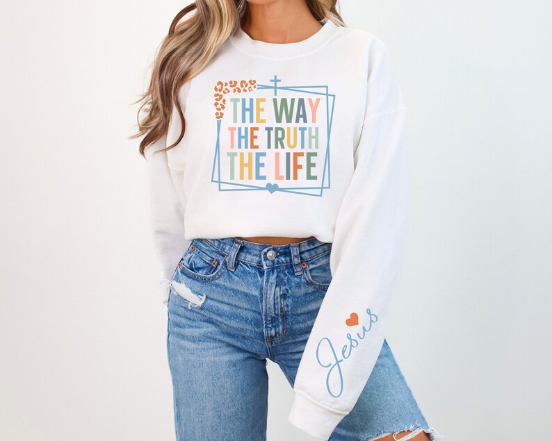 May include: White cropped sweatshirt with the text "The Way The Truth The Life" in a colorful frame and a cross. The left sleeve has the word "Jesus" in blue with a small red heart.
