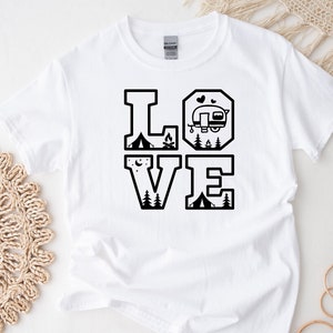 May include: White t-shirt with a black graphic design that says "LOVE" with camping and RV icons inside the letters.