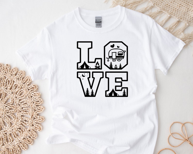 May include: White t-shirt with a black graphic design that says "LOVE" with camping and RV icons inside the letters.