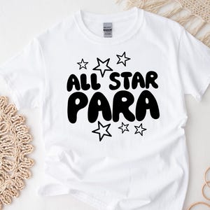 May include: White t-shirt with black text that reads "All Star Para" with stars around the text.