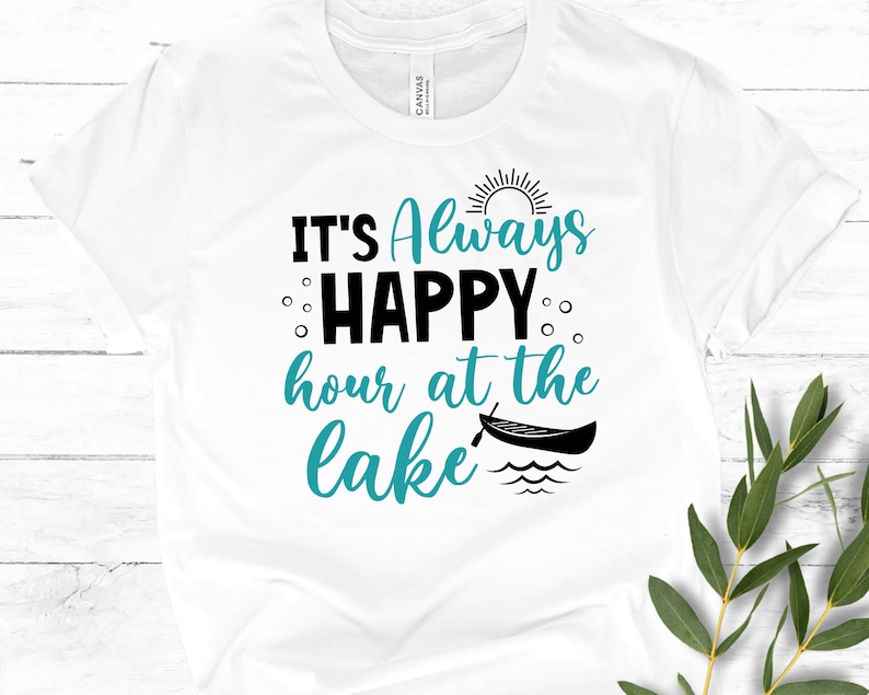 May include: White t-shirt with the text "It's Always Happy Hour at the Lake" in black and teal blue lettering. A sun and a canoe are also depicted on the shirt.