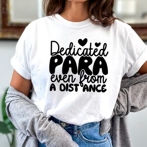 May include: White t-shirt with black text that reads "Dedicated Para even from a distance" with two small hearts above the word "Dedicated".