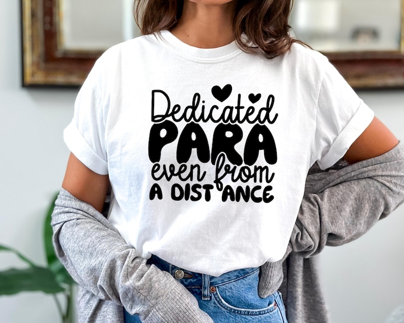 May include: White t-shirt with black text that reads "Dedicated Para even from a distance" with two small hearts above the word "Dedicated".