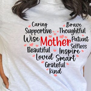 May include: White t-shirt with a heart-shaped design featuring the word "Mother" in red and a list of positive adjectives describing a mother, including caring, supportive, wise, brave, thoughtful, patient, selfless, beautiful, inspire, loved, smart, grateful, and kind.