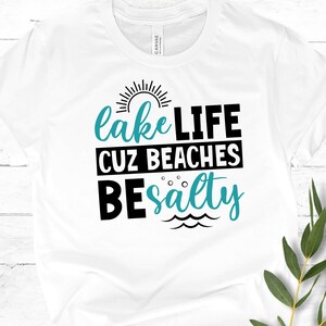 May include: White t-shirt with black text that reads "lake LIFE cuz beaches be salty" with a turquoise sun and waves graphic.