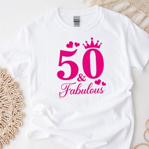 May include: White t-shirt with pink text that says "50 & Fabulous" with a crown and hearts.