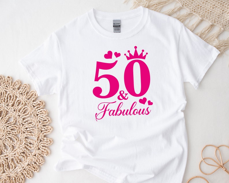 May include: White t-shirt with pink text that says "50 & Fabulous" with a crown and hearts.