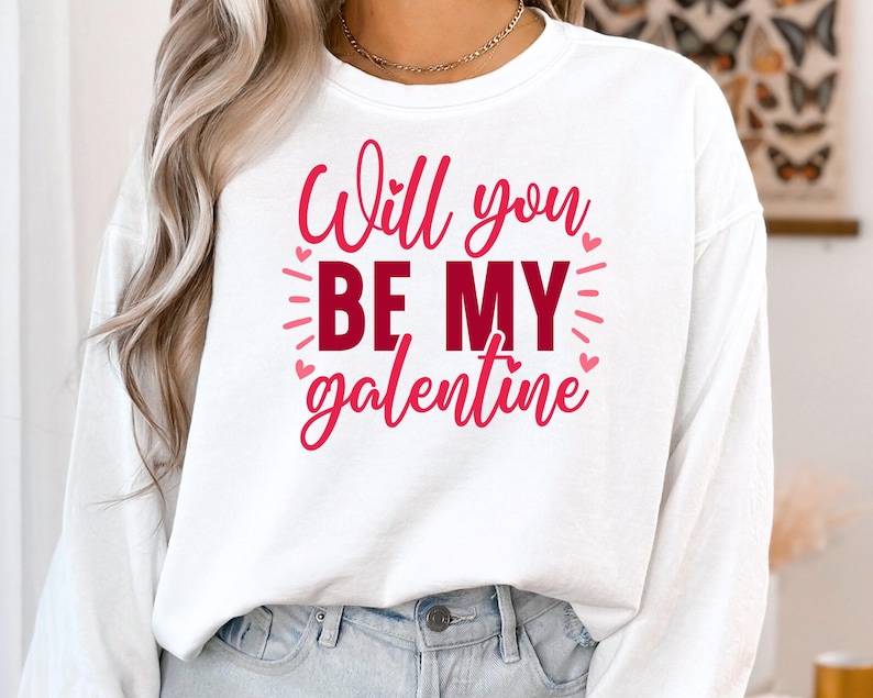 Op de afbeelding: Witte longsleeve met de tekst "Will you be my galentine" in roze letters.