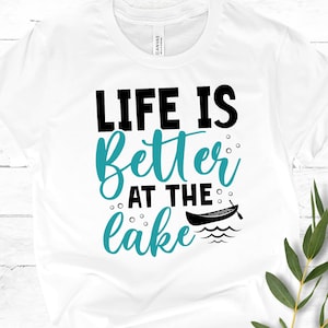 May include: White t-shirt with the text "Life is better at the lake" in black and teal blue lettering. A small black canoe with an oar is pictured next to the text.