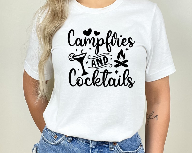 May include: White t-shirt with black text that reads "Campfires and Cocktails" with a graphic of a cocktail glass, two hearts, and a campfire.