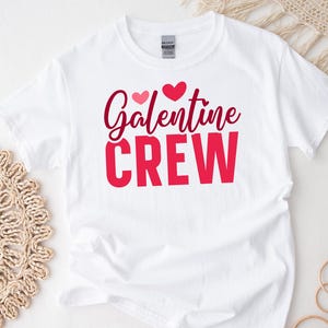 Op de afbeelding: Wit T-shirt met de tekst "Galentine Crew" in rode en roze letters met twee roze hartjes boven de tekst.