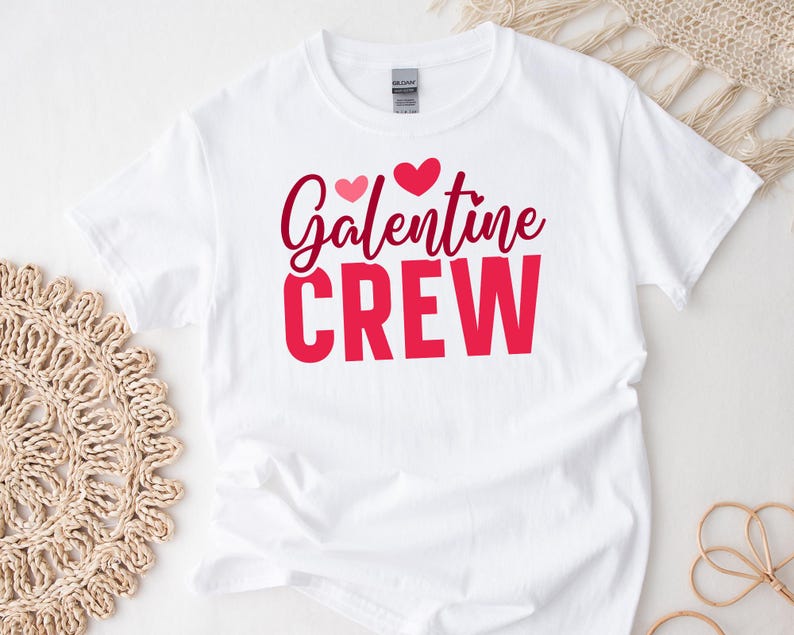 Op de afbeelding: Wit T-shirt met de tekst "Galentine Crew" in rode en roze letters met twee roze hartjes boven de tekst.