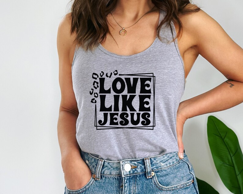 K&ouml;nnte beinhalten: Ein graues Tanktop mit dem Text "LOVE LIKE JESUS" in schwarzer, Retro-Schriftart in einem schwarzen Rahmen.