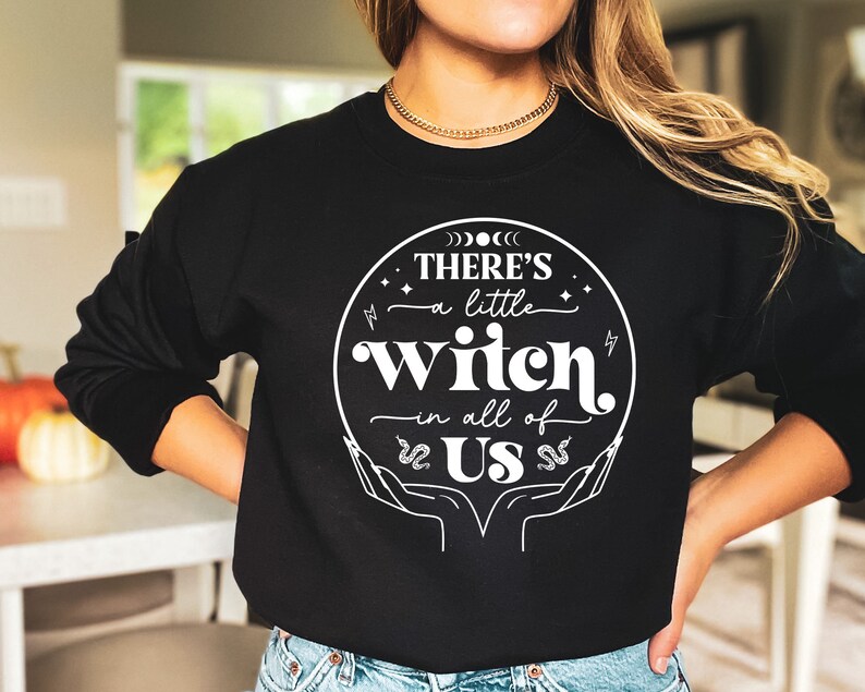 May include: Black sweatshirt with a white graphic design that says "There's a little witch in all of us" with a circle around the text and a snake design on each side of the text.