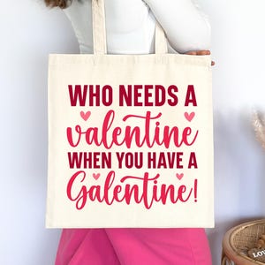 Op de afbeelding: Een witte tote bag met de tekst "Who needs a valentine when you have a Galentine!" in rode en roze letters. Er zijn kleine roze hartjes aan weerszijden van de tekst.