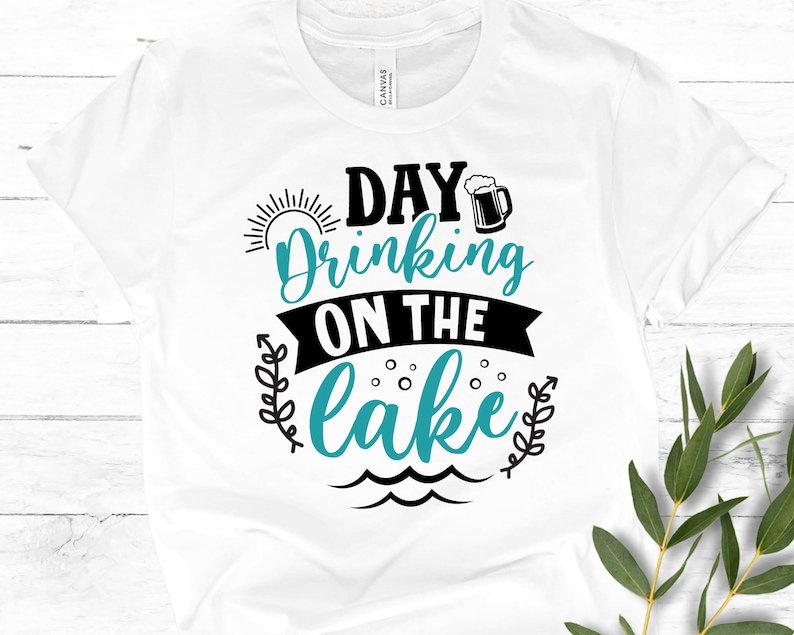 May include: White t-shirt with black text that reads "Day Drinking on the Lake" with a blue sun, a beer mug, and waves.