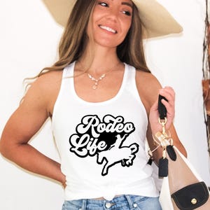 Op de afbeelding: Een wit tanktop met een zwarte afbeelding waarop "Rodeo Life" staat met een silhouet van een cowboy die een paard berijdt.