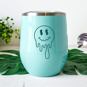 K&ouml;nnte beinhalten: Ein hellblauer Edelstahlbecher mit einem tropfenden Smiley-Gesicht-Design.