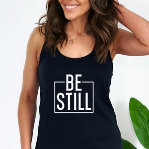 May include: Black tank top with a white box around the text "BE STILL".