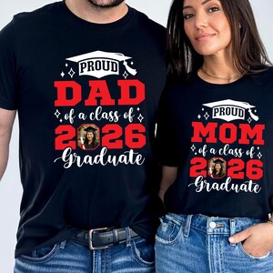 Peut inclure: T-shirts noirs avec l'inscription "PROUD DAD of a class of 2026 Graduate" et "PROUD MOM of a class of 2026 Graduate" en rouge et blanc. Chaque t-shirt pr&eacute;sente un motif de toque de dipl&ocirc;m&eacute; et une photo.