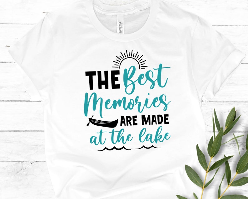 May include: White t-shirt with a teal blue graphic that says "The Best Memories Are Made at the Lake" with a sun and a canoe graphic.
