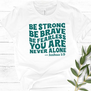 K&ouml;nnte beinhalten: Wei&szlig;es T-Shirt mit einer blaugr&uuml;nen Grafik, auf der steht: "Sei stark Sei mutig Sei furchtlos Du bist nie allein - Josua 1:9"