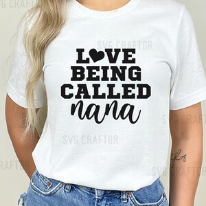 May include: White t-shirt with black text that reads "LOVE BEING CALLED nana" with a small black heart above the word "LOVE".
