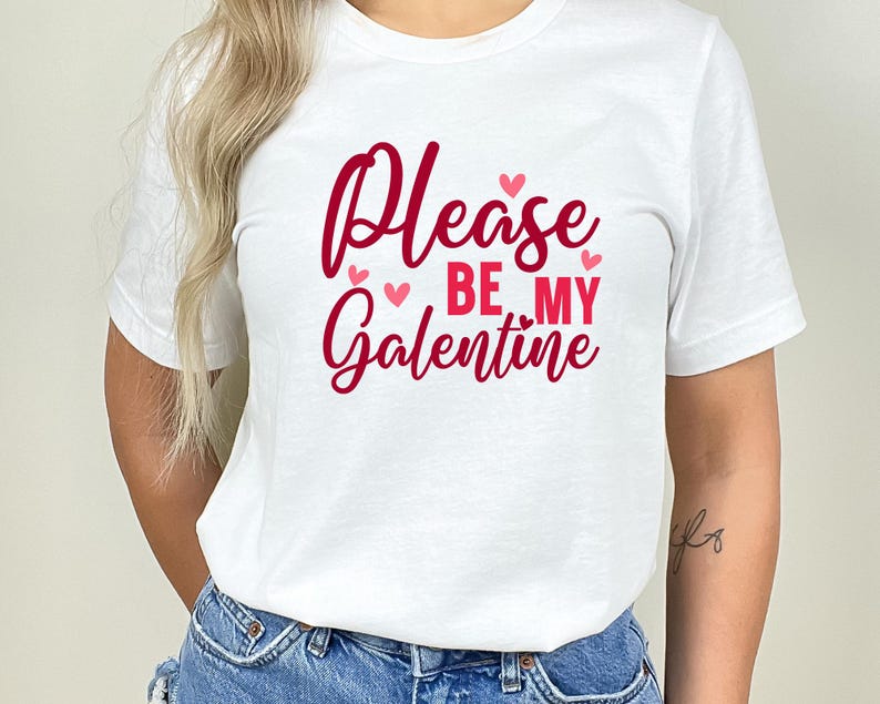 Op de afbeelding: Wit T-shirt met de tekst "Please be my Galentine" in rode letters met roze hartjes.
