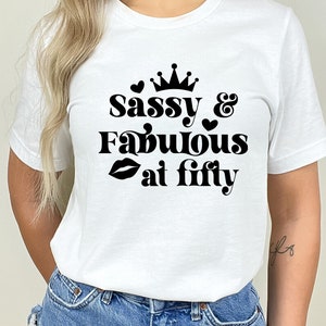 May include: White t-shirt with black text that reads "Sassy & Fabulous at Fifty" with a crown, hearts, and a lipstick graphic.