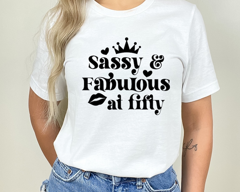 May include: White t-shirt with black text that reads "Sassy & Fabulous at Fifty" with a crown, hearts, and a lipstick graphic.