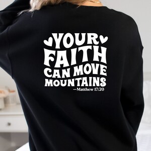 K&ouml;nnte beinhalten: Schwarzer Pullover mit wei&szlig;em Text, der "Your Faith Can Move Mountains - Matthew 17:20" lautet.