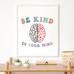 May include: A white framed print with the text "BE KIND TO YOUR MIND" in rainbow colors. A black and white illustration of a brain with one half filled with red hearts is in the center of the print.