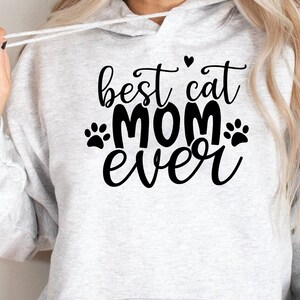 Pu&ograve; includere: Una felpa con cappuccio grigia con il testo "best cat mom ever" in lettere nere con impronte di zampe e un cuore.