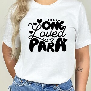 May include: White t-shirt with black text that reads "One Loved Para" with hearts around the text.